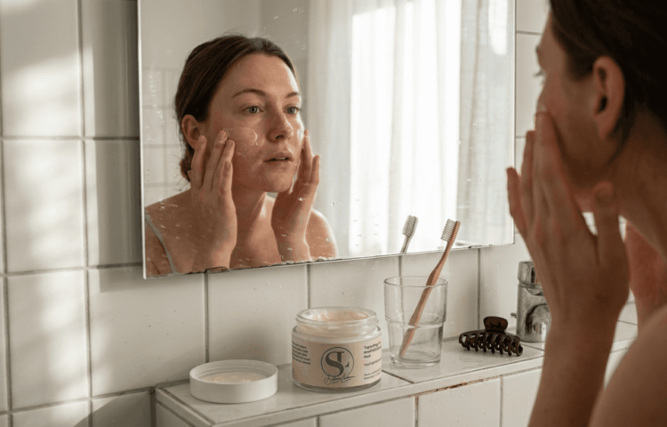 Eine Frau trägt am Waschbecken eine beruhigende Creme auf ihre gerötete Haut auf.